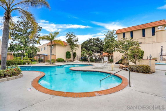 Outdoor swimming pool area with surrounding buildings and palm trees.
