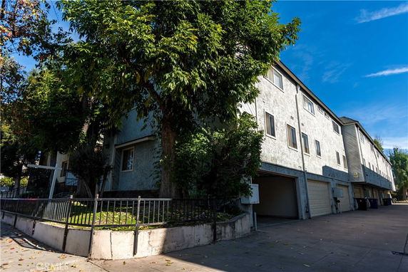 Front view of a multi-story building with garages and large trees.