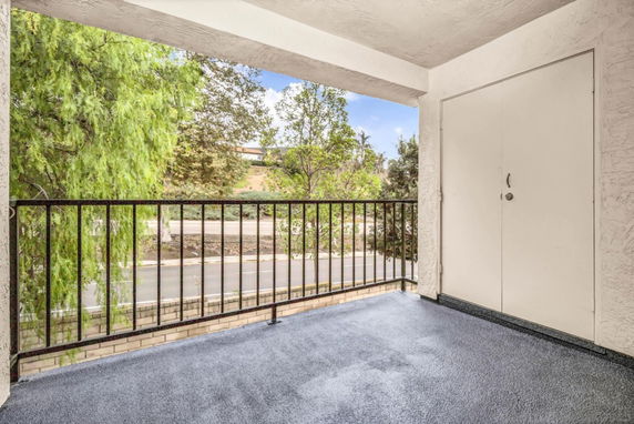 View from a balcony with railing overlooking trees and a road.