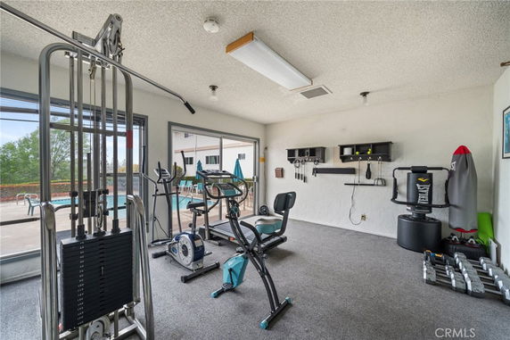 Home gym with exercise equipment and view of a swimming pool through a glass door.