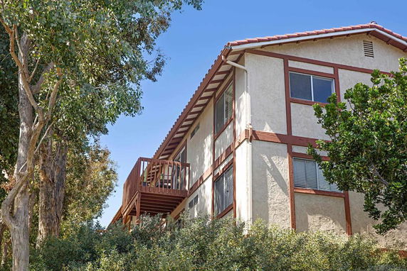 Angled view of a two-story building with a balcony and trees surrounding it.