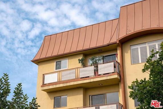 Front view of an apartment building with balconies and a sloped roof.