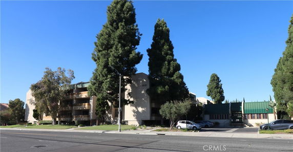 Front view of a multi-story apartment building with green rooftops and surrounding trees.