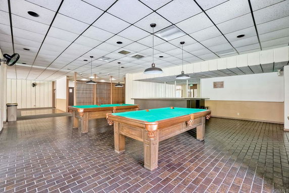 Indoor recreation area with two billiard tables and hanging lights.