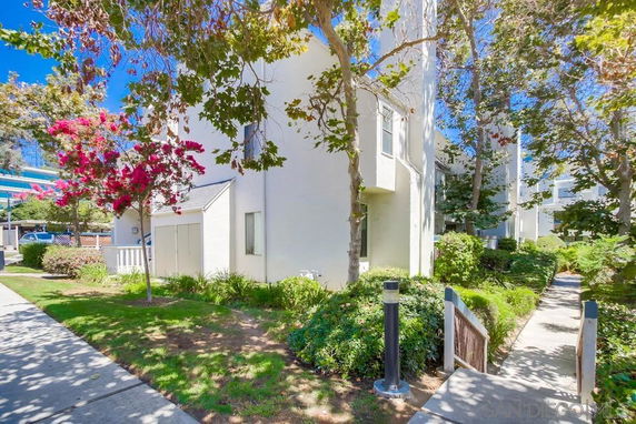 Front view of a white multi-story residential building with trees and shrubs in front.