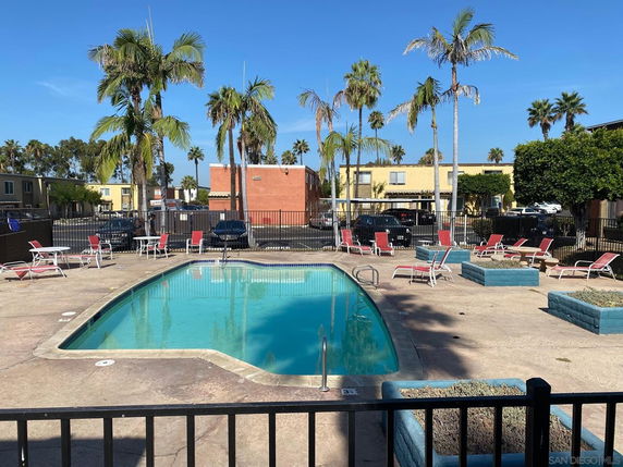 Outdoor area with a swimming pool surrounded by lounge chairs and palm trees.