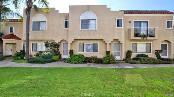 Front view of a two-story house with cream stucco exterior and red tile roof accent.