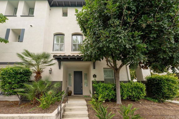Front view of a multi-story house with a small porch and surrounding greenery.