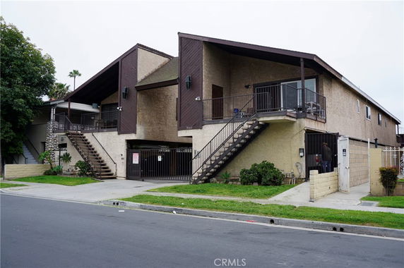 Front view of a two-story residential building with outdoor staircases and gated entrance.