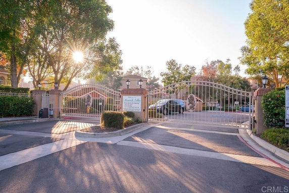 Entrance view of a gated community with a decorative iron gate and surrounding trees.