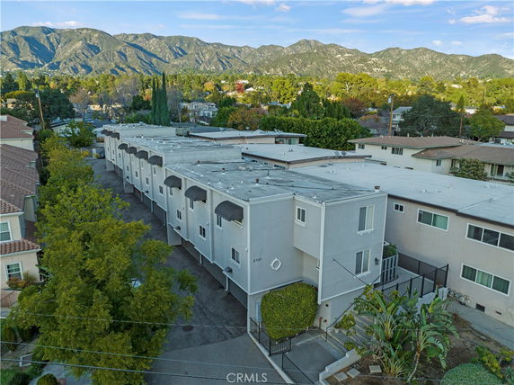 Front view of a row of two-story buildings with flat roofs and awnings, surrounded by trees and mountain scenery.