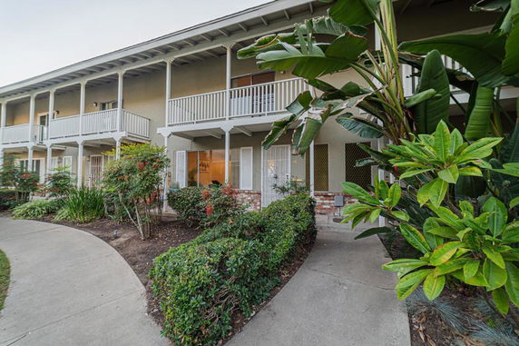Front view of a two-story apartment building with balconies and surrounding greenery.