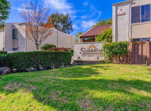 Front view of a residential building complex with a sign and surrounding greenery.