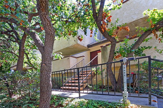 Front view of a multi-story residential building with a staircase and trees in the foreground.