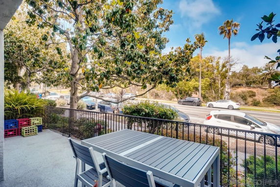 Outdoor view showing a table and chairs on a patio overlooking a street with trees and parked cars.