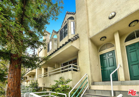 Front view of a multi-story building with green doors and a balcony.
