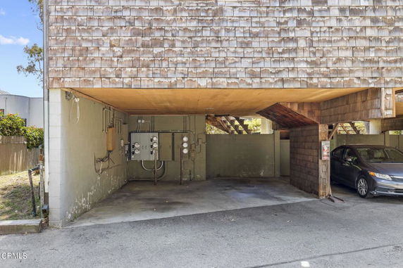 Covered outdoor parking area with a parked car and utility meters on the wall.