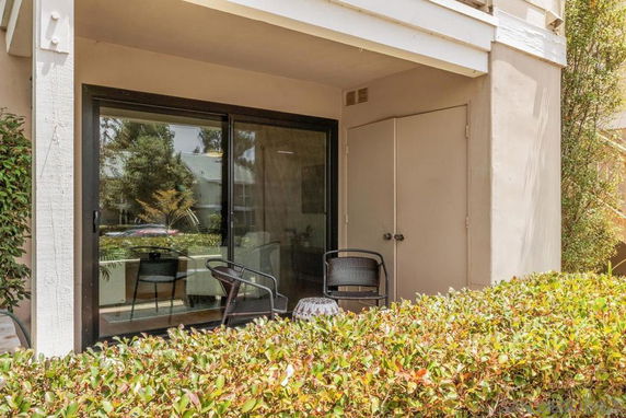 Front view of a building with a patio and sliding glass door, partially obscured by shrubs.