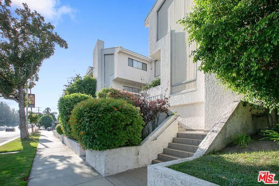 Front view of a multi-story building with a sloped entrance and surrounding shrubs.