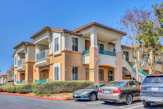 Front view of a two-story residential building with balconies and parked cars.