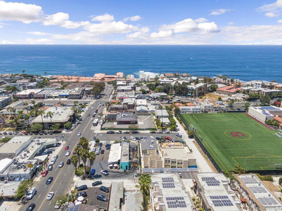 Panoramic view of a coastal city with roads, buildings, and a sports field near the ocean.