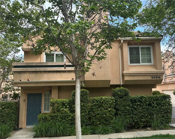 Front view of a two-story house with a blue front door and shrubs in front.