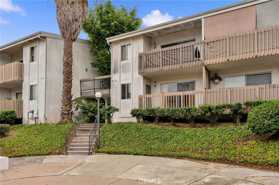 Front view of a multi-story residential building with balconies and stairs leading to the entrance.