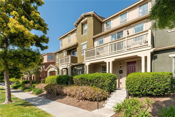 Front view of a three-story townhouse with balconies and a staircase leading to the entrance.