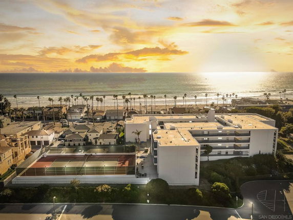 Aerial view of a coastal area with a large building and tennis courts near the beach.