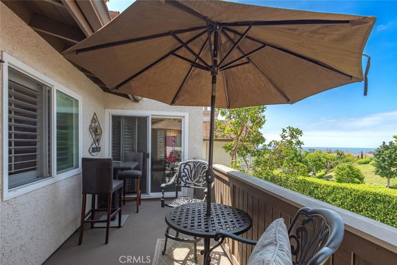 Outdoor balcony with seating and umbrella, offering a view of the landscape and distant ocean.