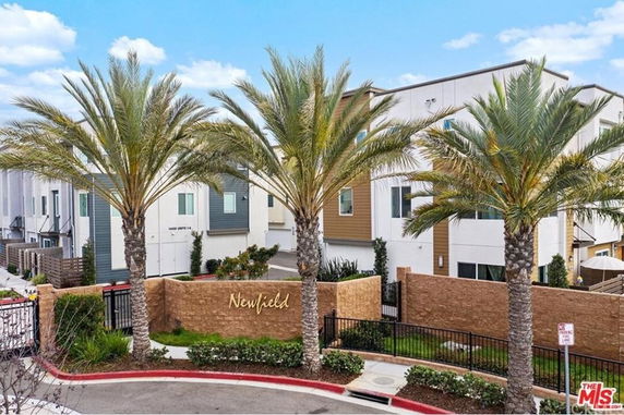 Front view of a modern multi-story residential building with palm trees and a decorative wall.