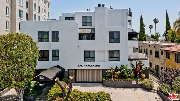 Front view of a multi-story building named De Voltaire with a gated entrance.