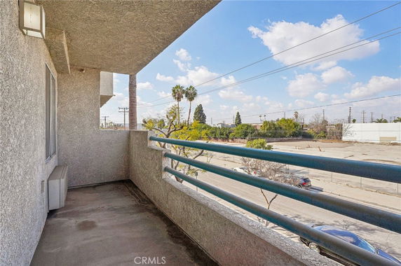 Balcony view with railing overlooking a street and trees in the distance.