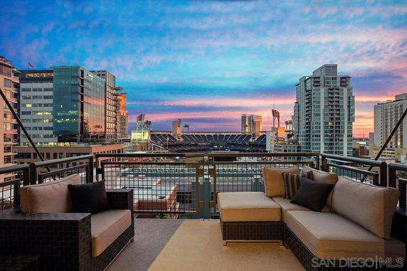 Panoramic view from a balcony overlooking city buildings and a stadium at sunset.