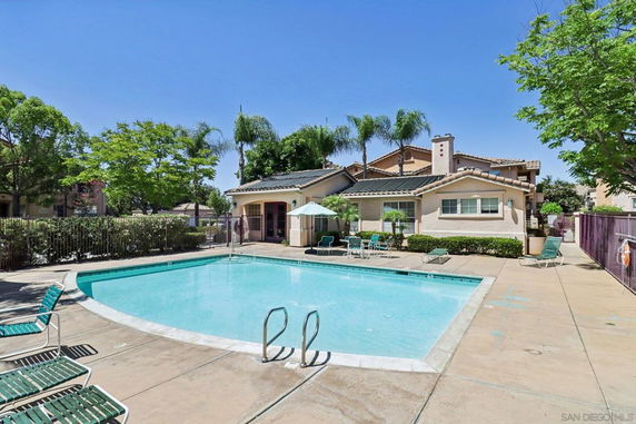 Outdoor swimming pool with surrounding deck chairs and a house in the background.