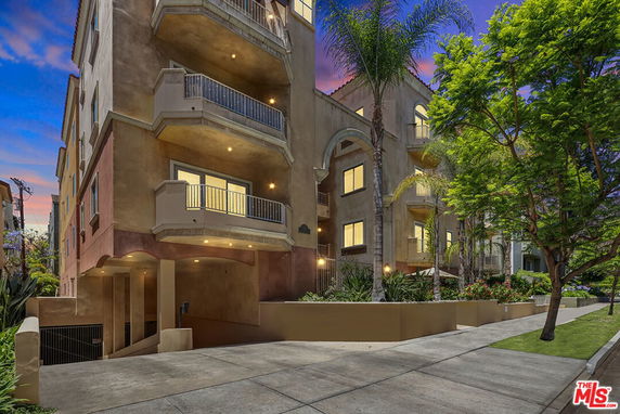 Front view of a multi-story apartment building with balconies and landscaped surroundings.