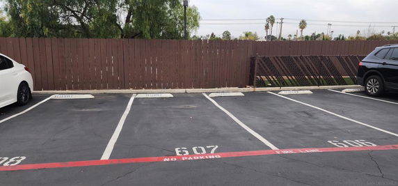 Outdoor parking spaces with marked reserved slots next to a wooden fence.