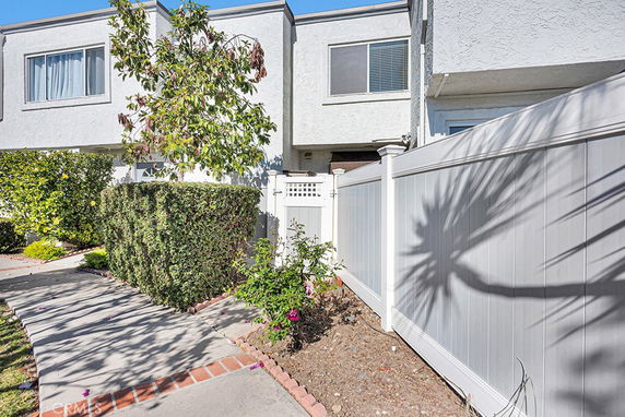 Front view of a two-story residential building with a white fence and a pathway.