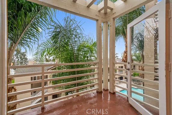 Balcony with wooden railing overlooking palm trees and a swimming pool.