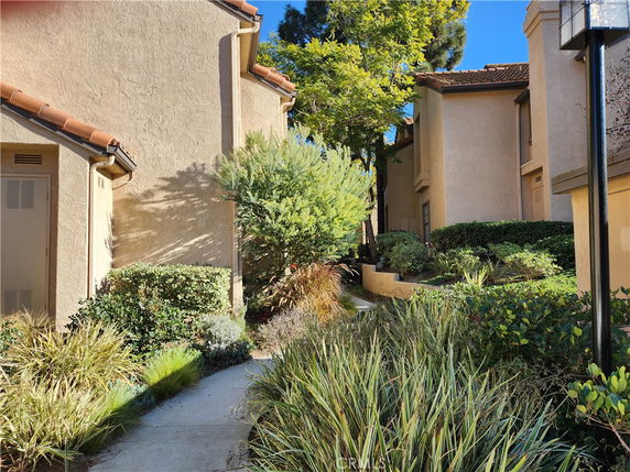 Pathway between buildings with garden areas and trees.