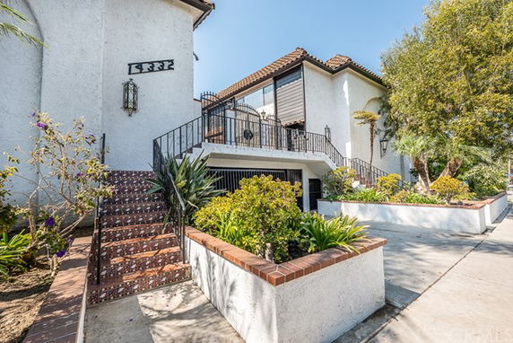Front view of a multi-story house with external stairs and landscaped garden.