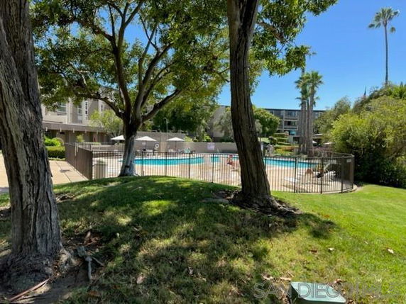 Outdoor area with a fenced swimming pool surrounded by trees and grass.