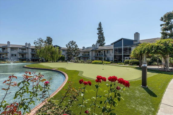 View of multi-story residential buildings with balconies near a landscaped pond and a putting green.
