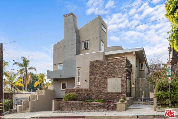 Front view of a modern multi-story house with a stone accent wall and a chimney.