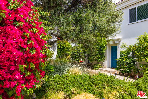 Front view of a house with a blue door and surrounding greenery.