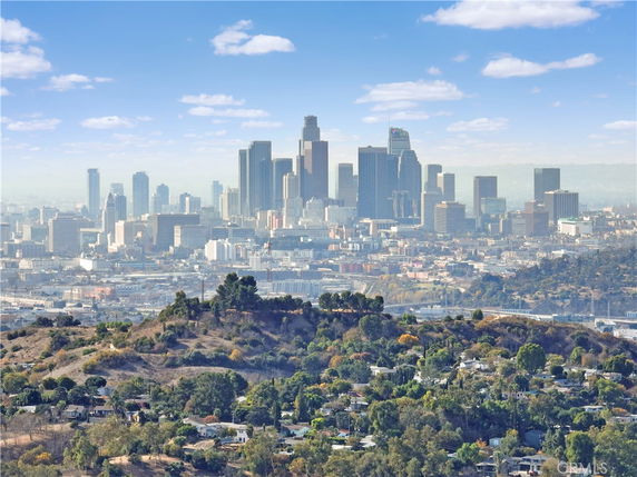 Panoramic view of a city skyline with hills and green areas in the foreground.