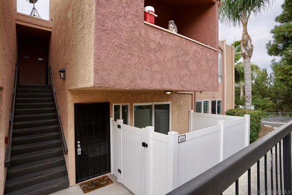 Front view of a two-story building with an outdoor staircase and a fenced-in porch area.