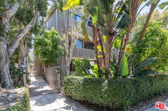 Front view of a multi-story building with balconies and lush vegetation.