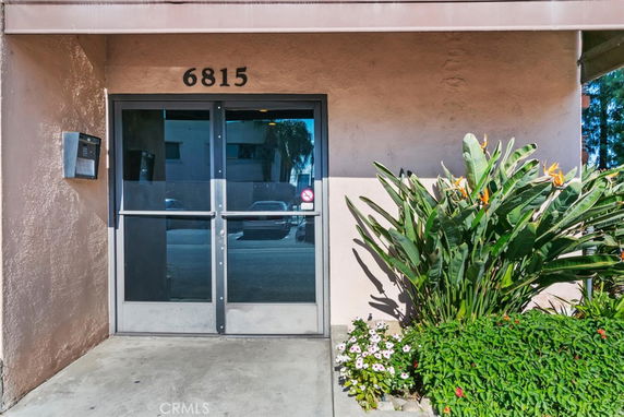 Front entrance of a building with glass doors and plants.