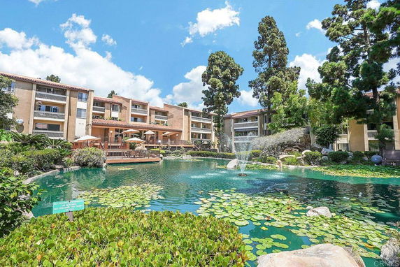 Front view of a multi-story residential building with balconies and a pond with water lilies in front.